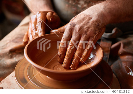 Close-up hands of a male potter in apron making a vase from clay, selective focus Close-up hands of a male potter in apron making a vase from clay, selective focus 40481212