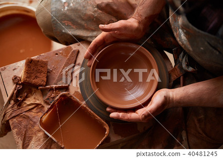 Close-up hands of a male potter in apron making a vase from clay, selective focus Close-up hands of a male potter in apron making a vase from clay, selective focus 40481245