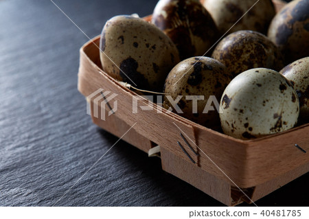 Quail eggs in a box on a dark black background, top view, selective focus, backlight. Quail eggs in a box on a dark black background, top view, selective focus, backlight. 40481785