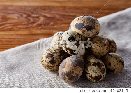 Quail eggs arranged in pyramid on a napkin over a wooden table, close-up, selective focus. 40482145