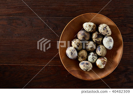 Fresh quail eggs in a wooden plate on a dark wooden background, top view, close-up Fresh quail eggs in a wooden plate on a dark wooden background, top view, close-up 40482309