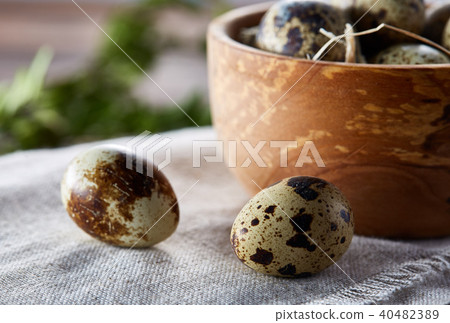 Bowl with eggs quail, eggs on a homespun napkin, boxwood on wooden background, close-up, selective Bowl with eggs quail, eggs on a homespun napkin, boxwood on wooden background, close-up, selective 40482389
