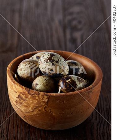 Fresh quail eggs in a wooden bowl on a dark wooden background, top view, close-up 40482837
