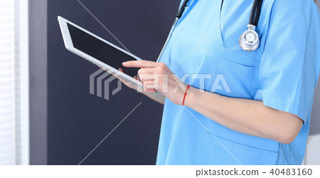 Woman doctor using tablet computer while standing straight in hospital office, closeup. Healthcare Woman doctor using tablet computer while standing straight in hospital office, closeup. Healthcare 40483160