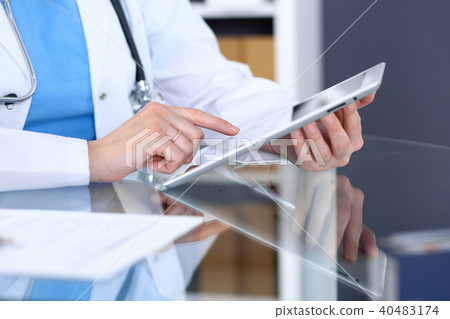 Woman doctor using tablet computer while sitting at the glass table in hospital office, closeup 40483174