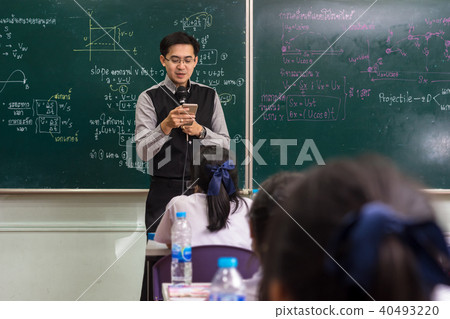 Asian teacher using the smart mobile phone for Giving Lesson over the the physics formular in thai laguage on black board in school classroom, school education concept, The teacher wrote himself 40493220