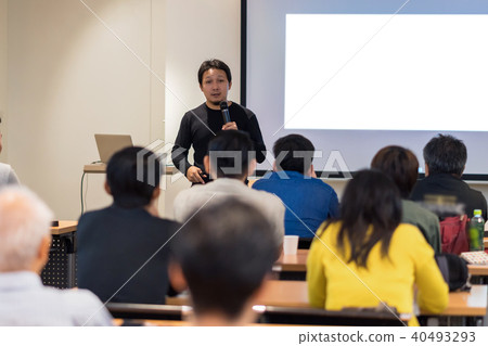 Asian Speaker with casual suit on the stage in low light over the presentation screen in the business or education seminar Asian Speaker with casual suit on the stage in low light over the presentation screen in the business or education seminar 40493293