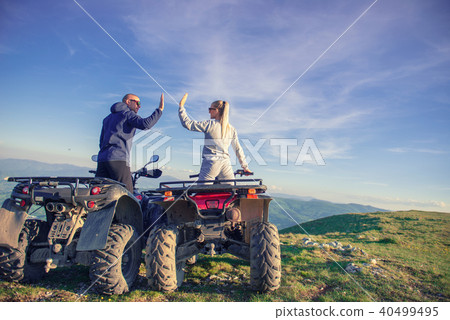 Rear view of young pair near atv. Man is showing something in distance to her girlfriend. 40499495