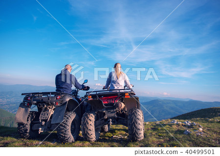 Rear view of young pair near atv. Man is showing something in distance to her girlfriend. 40499501