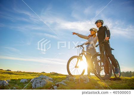 Biker couple with mountain bike pointing in distance at countryside 40500003