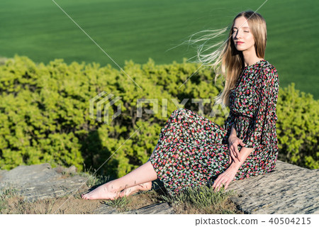 Beautiful girl in dress poses on rock in nature 40504215