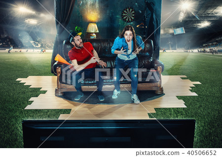 Ardent fans are sitting on the sofa and watching TV in the middle of a football field. 40506652