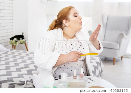 Concentrated plump woman polishing her nails 40508155