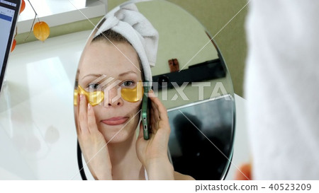 attractive business woman applying cosmetic facial spots at home, talking on the phone 40523209