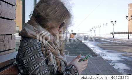 Woman Using Smartphone Relaxes on the Bench in Beautiful Park. Young Woman in making gestures on 40523273