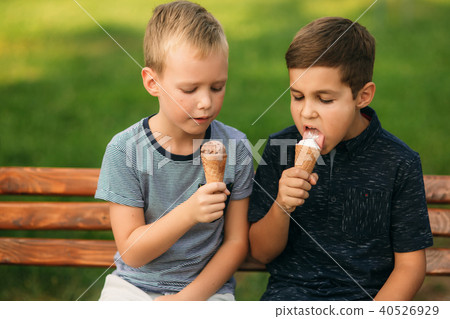 Two childre sitting on the bench and eating ice cream Two childre sitting on the bench and eating ice cream 40526929