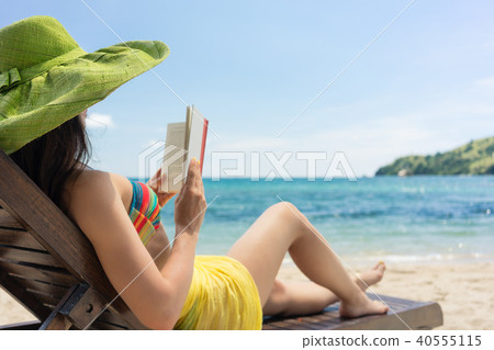Young beautiful woman reading a book at the beach in a sunny day Young beautiful woman reading a book at the beach in a sunny day 40555115