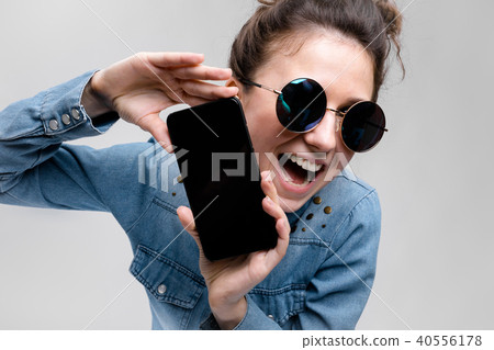 Young brunette girl in round glasses. Hairs are gathered in a bun. Girl with a black phone. 40556178