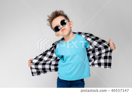 A handsome boy in a plaid shirt, blue shirt and jeans stands on a gray background. The boy is A handsome boy in a plaid shirt, blue shirt and jeans stands on a gray background. The boy is 40557147