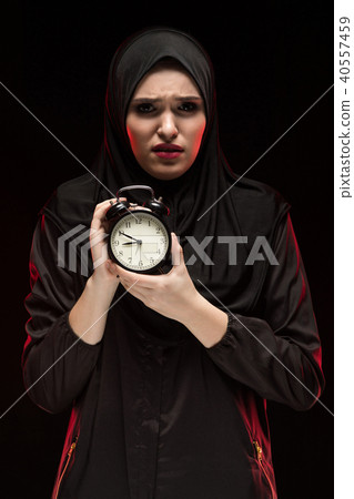 Portrait of beautiful serious scared frightened young muslim woman wearing black hijab holding alarm Portrait of beautiful serious scared frightened young muslim woman wearing black hijab holding alarm 40557459