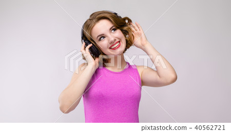 Charming young girl in pink dress on gray background. Young girl with headphones smiling 40562721
