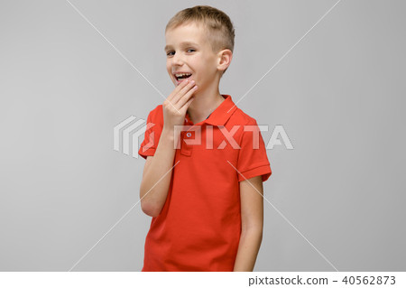 Portrait of little blonde happy smiling caucasian boy in orange t-shirt with hand near his face on 40562873