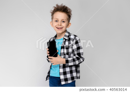 A handsome boy in a plaid shirt, blue shirt and jeans stands on a gray background. The boy is A handsome boy in a plaid shirt, blue shirt and jeans stands on a gray background. The boy is 40563014