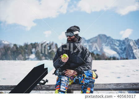 Bearded snowboarded in sunglass mask, at the ski resort on the background of mountains and blue sky Bearded snowboarded in sunglass mask, at the ski resort on the background of mountains and blue sky 40563017