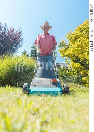 Active senior man smiling while using a grass cutting machine in the garden 40563957