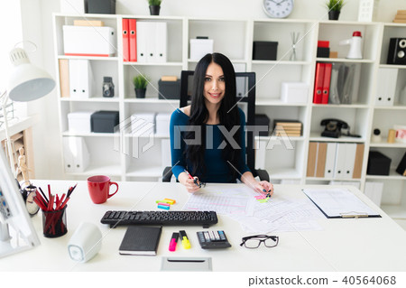 A young girl sits in the office at the table, holds a pen in her hand and fills out the documents. A young girl sits in the office at the table, holds a pen in her hand and fills out the documents. 40564068
