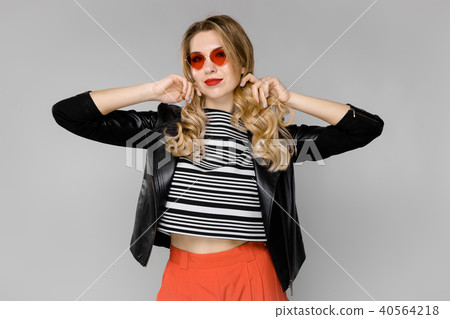 A beautiful girl in red glasses holds her blond hair with her hands A beautiful girl in red glasses holds her blond hair with her hands 40564218