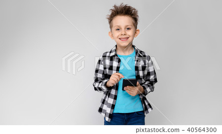 A handsome boy in a plaid shirt, blue shirt and jeans stands on a gray background. The boy is 40564300