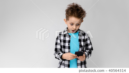 A handsome boy in a plaid shirt, blue shirt and jeans stands on a gray background. The boy is 40564314