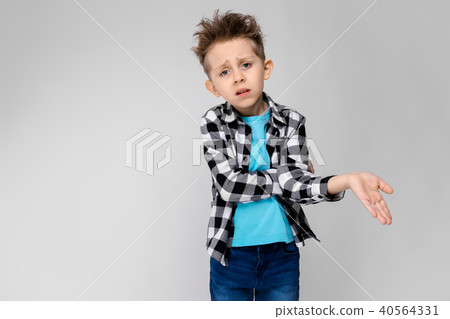 A handsome boy in a plaid shirt, blue shirt and jeans stands on a gray background. The boy folded 40564331
