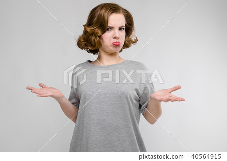 Charming young girl in a gray T-shirt on a gray background. The girl spread her arms Charming young girl in a gray T-shirt on a gray background. The girl spread her arms 40564915