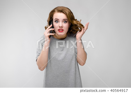 Charming young girl in a gray T-shirt on a gray background. The girl speaks by phone Charming young girl in a gray T-shirt on a gray background. The girl speaks by phone 40564917