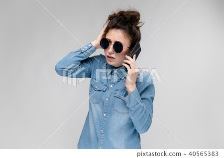 Young brunette girl in round glasses. Hairs are gathered in a bun. Girl with a black phone. The girl 40565383