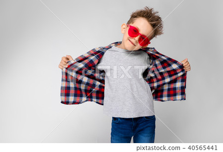 A handsome boy in a plaid shirt, gray shirt and jeans stands on a gray background. A boy in red 40565441