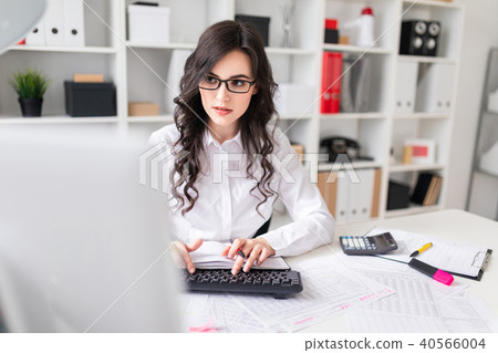 A young girl is working at the computer in the office and holds a pen and notebook in her hand. 40566004