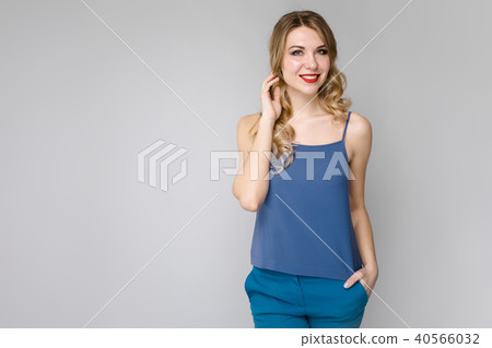 Charming girl with white long curly hair. Girl in a blue top and blue pants on gray background 40566032