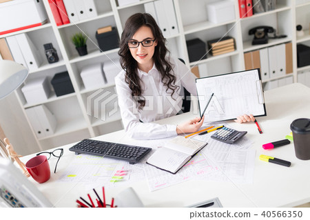 A beautiful young girl is sitting at a table in the office and pointing a pencil at the information 40566350