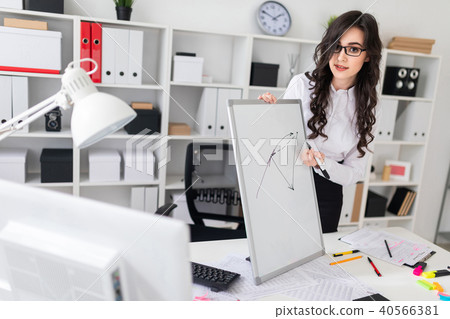 A beautiful young girl stands near an office desk and draws a magnetic marker on the magnetic board. 40566381