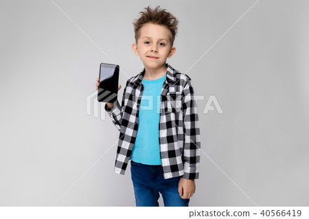 A handsome boy in a plaid shirt, blue shirt and jeans stands on a gray background. The boy is 40566419