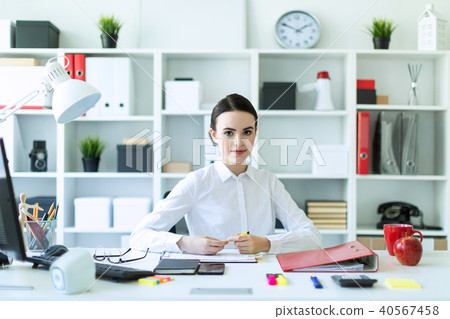 A young girl in the office sits at a table and holds a pen in her hands. 40567458