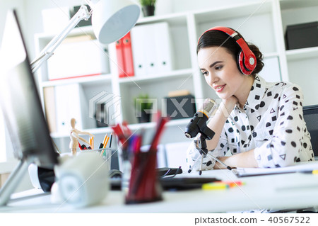 Beautiful young girl sitting in headphones and with microphone at table in office and talking. 40567522