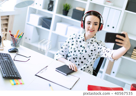Beautiful young girl sitting in headphones at desk in office and taking pictures of herself on the 40567535