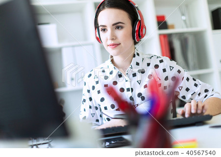 Beautiful young girl sits in headphones at desk in office, holds a notebook in her hand and prints 40567540