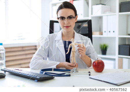 A beautiful young girl in a white robe is sitting at a table and holding a wooden figure of a man in 40567562
