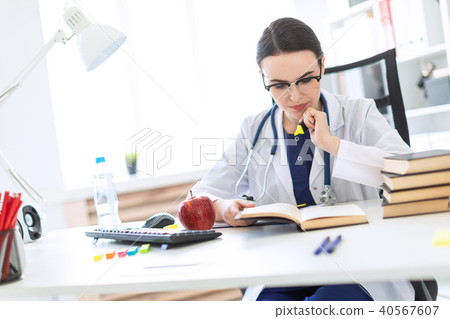 A beautiful young girl in a white robe is sitting at the computer desk with a marker and a book. A 40567607