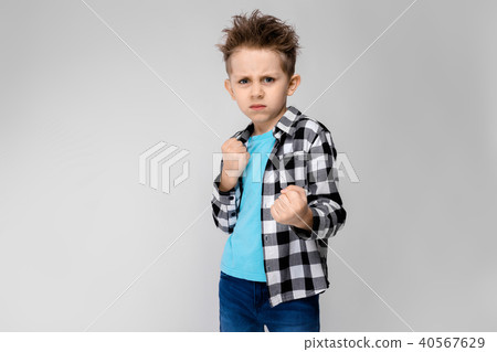 A handsome boy in a plaid shirt, blue shirt and jeans stands on a gray background. The boy stands in 40567629